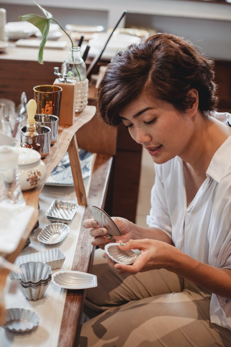 Young attentive ethnic female shopper choosing decorative molds near wooden shelves with assorted kitchen items in store